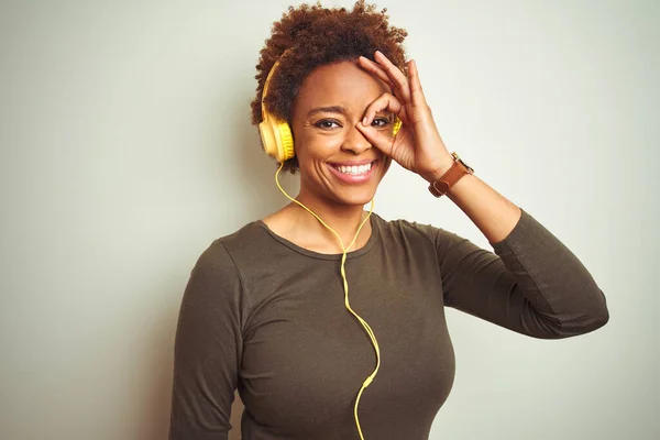 African american woman wearing headphones listening to music over isolated background doing ok gesture with hand smiling, eye looking through fingers with happy face.