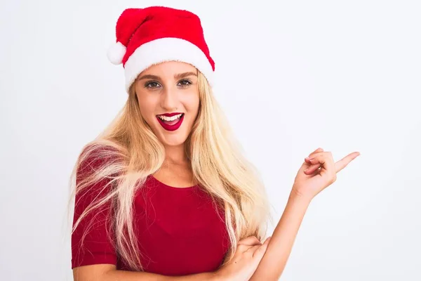 若いです美しいです女性身に着けていますクリスマスサンタ帽子上の孤立した白い背景に大きな笑顔で顔 カメラを見て側に手と指で指して — ストック写真