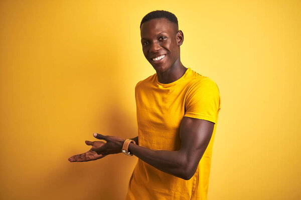 Young african american man wearing casual t-shirt standing over isolated yellow background Inviting to enter smiling natural with open hand