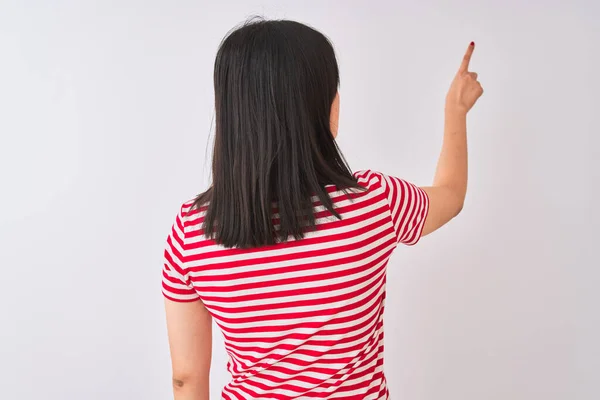 Young beautiful chinese woman wearing red striped t-shirt over isolated white background Posing backwards pointing ahead with finger hand