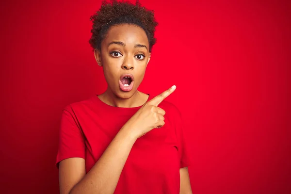 Young beautiful african american woman with afro hair over isolated red background Surprised pointing with finger to the side, open mouth amazed expression.