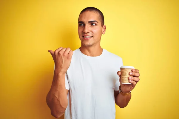 若いですハンサムな男飲みます取りますコーヒーのガラス以上黄色隔離された背景指すと表示しますとともに親指で側まで幸せな顔笑顔 — ストック写真