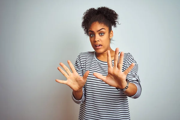 African american woman wearing navy striped t-shirt standing over isolated white background afraid and terrified with fear expression stop gesture with hands, shouting in shock. Panic concept.