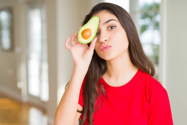 Beautiful young woman holding healthy avocado sending a kiss — Stock Photo, Image