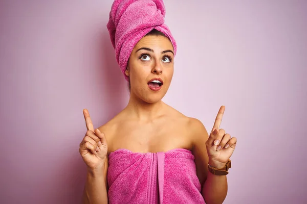 若いです美しいです女性身に着けているタオル後シャワーで隔離されたピンクの背景驚きと驚きを見上げと指差し指と上げ腕 — ストック写真