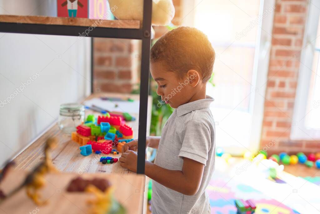 Beautiful african american toddler standing playing with small building blocks on shelving at kindergarten