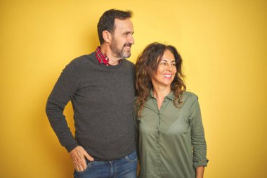 Güzel orta yaşlı çift, izole edilmiş sarı arka planda. Yüzlerinde gülümseme, doğal bir ifade ile yan yana bakıyorlar. Kendinden emin gülen.