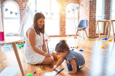 Genç, güzel öğretmen ve bebek yerde oturup anaokulunda fırçayla oynuyorlar.