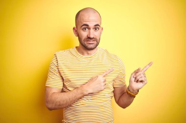 Sakallı, sarı tişörtlü, sakallı genç bir adam. İzole edilmiş sarı arka plan. Endişeli ve gergin.