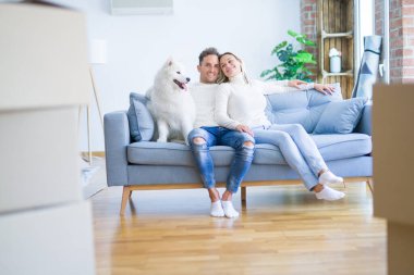 Karton kutular etrafında yeni evde kanepede oturan köpek ile genç güzel çift