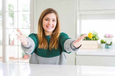 Young beautiful plus size woman wearing casual striped sweater smiling cheerful offering hands giving assistance and acceptance.