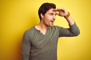 İzole edilmiş sarı arka planda dikilen sıradan tişört giyen yakışıklı genç adam çok mutlu ve tebessüm ediyor. Konsept aranıyor.