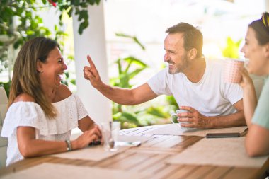 Güzel bir aile terasta oturmuş kahve içiyor, konuşuyor ve gülümsüyor.