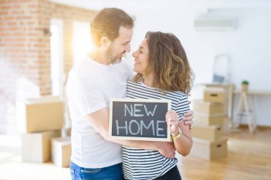 Orta yaş Senior çift yeni bir eve hareket, yeni bir ev metin ile bir tahta tutan Apartmant aşık mutlu gülümseyen