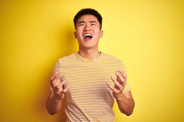 Asyalı genç bir Çinli tişört giyiyor. Sarı arka planda duruyor. Deli gibi bağırıyor, bağırıyor, agresif bir ifade ve kollarla bağırıyor. Hayal kırıklığı konsepti.