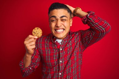 İzole edilmiş kırmızı arka planda ayakta duran genç Brezilyalı bir adam elleri başının üstünde, utanç ve şaşkınlık dolu, sinirli ve hayal kırıklığına uğramış bir halde. Hata için korku ve üzüntü.