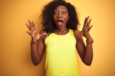 Genç Afro-Amerikan kadın tişört giyip izole edilmiş sarı arka planda dikilmiş çılgın ve başarıyı kutlarken kollarını kaldırmış ve gözleri açık bir şekilde heyecanla haykırıyordu. Kazanan konsept