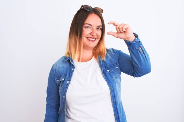 İzole edilmiş beyaz arka planda duran kot gömlekli güzel bir kadın gülümsüyor ve kendine güvenen el hareketleriyle küçük beden işareti yapıyor parmaklarıyla bakıyor ve kameraya bakıyor. Ölçü kavramı.
