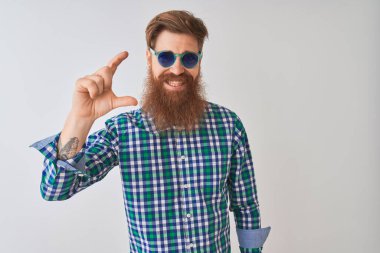 Genç, kızıl saçlı, günlük gömlek ve güneş gözlüğü takan, beyaz arka planda gülümseyen ve el hareketleriyle küçük boy işareti yapan, parmaklarıyla kameraya bakan genç bir İrlandalı. Ölçü kavramı.