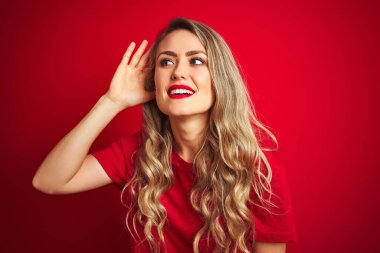 Genç ve güzel bir kadın kırmızı izole edilmiş arka plan üzerinde dikilmiş dedikodu ya da dedikodulara kulak misafiri olarak gülümsüyor. Sağırlık kavramı.