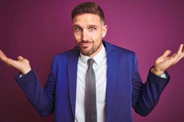 Mor arka plan üzerinde genç ve yakışıklı bir iş adamı. Kolları ve elleri havada, kafası karışık bir yüz ifadesi. Şüphe kavramı.