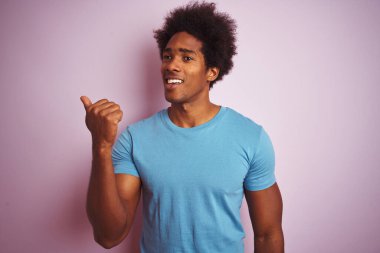 Afro saçlı, mavi tişörtlü, izole edilmiş pembe arka planda gülümseyen ve baş parmağıyla yüzünü gösteren Afro-Amerikan bir adam..