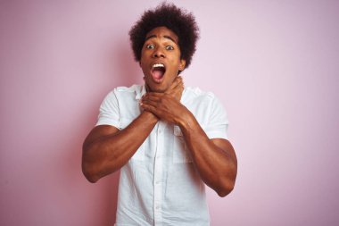 Afro saçlı, beyaz tişörtlü genç bir Amerikalı izole edilmiş pembe arka planda durup bağırıyor ve boğuluyor çünkü acı verici bir boğulma var. Sağlık problemi. Boğulma ve intihar konsepti.