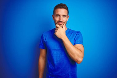 Mavi izole edilmiş arka plan üzerine günlük tişört giyen genç yakışıklı adam kameraya kollarını kavuşturup gülümseyerek ve çenesini kaldırarak bakıyor. Olumlu düşünüyorum..