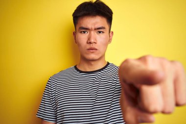 Çizgili tişört giyen Asyalı genç adam izole edilmiş sarı arka planda dikiliyor. Kamerayı işaret ediyor. Ve sen, el işareti, ön taraftan pozitif ve kendinden emin bir hareket.