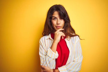 Sarı izole arka planda kırmızı tişört ve çizgili tişört giyen genç ve güzel bir kadın kameraya kollarını kavuşturup gülümseyerek ve çenesini kaldırarak bakıyor. Olumlu düşünüyorum..