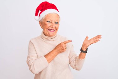 Yaşlı gri saçlı kadın, izole edilmiş beyaz arka plan üzerinde Crhistmas Noel Baba şapkası takıyor kameraya hayret ediyor ve gülümsüyor..