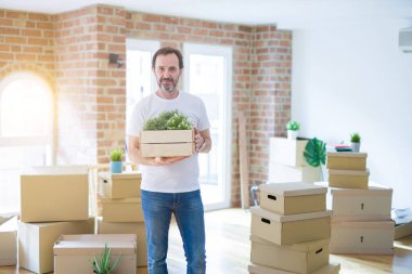 Orta yaşlı bir adam yeni bir eve taşınıyor. Karton kutuları paketliyor. Yüzünde kendine güvenen bir ifade var.