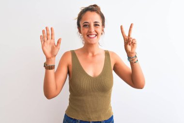 Genç kızıl saçlı kadın izole edilmiş arka planda topuz takıyor ve yedi numaralı parmaklarıyla işaret ederken kendinden emin ve mutlu gülümsüyor..