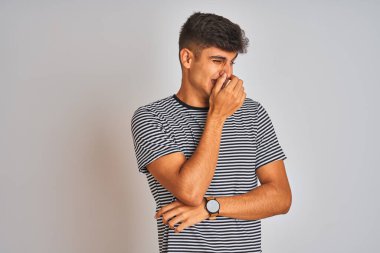 İzole edilmiş beyaz arka planda donanma tişörtü giyen genç Hintli adam pis ve iğrenç bir koku alıyor. Nefesini burnunda tutuyor. Kötü koku konsepti.