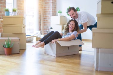 Orta yaş yaşlı romantik çift eğlenmek, karton içinde sürme, heyecanlı ve yeni bir eve taşımak için mutlu gülümseyen