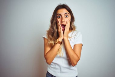 İzole edilmiş arka plan üzerinde gündelik beyaz tişört giyen genç ve güzel bir kadın. Korkmuş ve şok olmuş, şaşırmış ve şaşırmış bir halde.