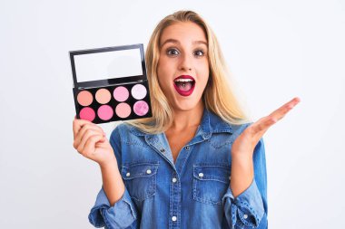 Güzel, sarışın, makyajlı genç bir kadın izole edilmiş beyaz arka planda mutlu ve heyecanlı duruyor. Kazanan ifade zaferi büyük bir gülümsemeyle kutluyor ve ellerini kaldırıyor.