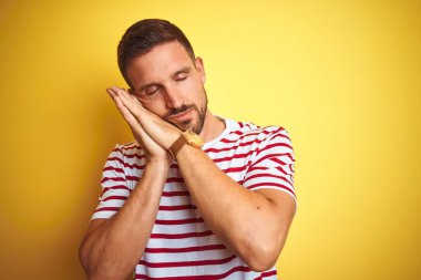 Sarı renkli tişört giyen yakışıklı genç adam izole edilmiş arka planda uyur, yorgun düşler görür ve elleri ile birlikte poz verir, kapalı gözlerle gülümserdi..