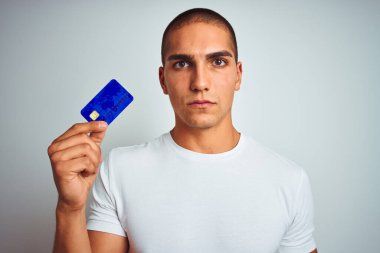 Genç, yakışıklı bir adam kredi kartını beyazların izole edilmiş geçmişinde tutuyor. Akıllı bir yüz ifadesiyle ciddi olduğunu düşünüyor.