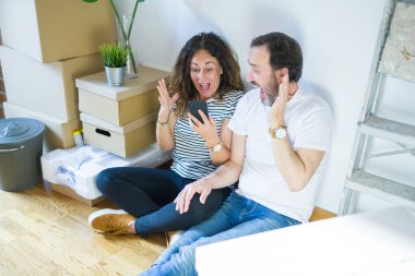 Orta yaşlı çift akıllı telefon kullanarak yeni bir eve taşınıyor. Çok mutlu ve heyecanlı, kazanan yüz ifadesi zaferi büyük bir gülümsemeyle kutluyor ve ellerini kaldırıyor.