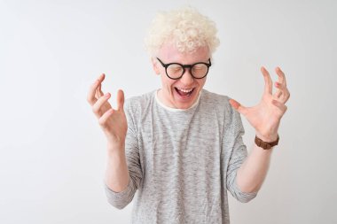 Genç albino sarışın adam çizgili tişört ve gözlüklerle izole edilmiş beyaz arka planda çılgın ve çılgın bir başarıyı kollarını kaldırarak ve kapalı gözlerle heyecanla haykırarak kutluyor. Kazanan konsept