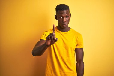 Genç, Afro-Amerikalı bir adam, günlük tişört giymiş, sarı arka planda dikiliyor, parmağını kaldırmış, kızgın bir ifadeyle işaret ediyor, hiçbir hareket göstermiyor.