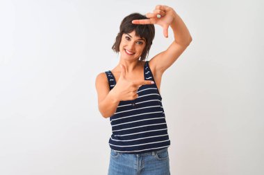 Young beautiful woman wearing striped t-shirt standing over isolated white background smiling making frame with hands and fingers with happy face. Creativity and photography concept.