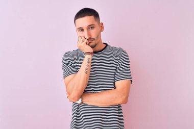 Pembe yalıtılmış arka plan üzerinde duran çizgili tişört giyen yakışıklı genç adam kollarını kavuşturarak depresyondan sıkılmış ve yorgun görünüyor..