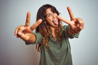 Gri izole arka planda duran yeşil tişörtlü genç ve güzel bir kadın. İki elini de göstererek gülümseyerek zafer işareti yapıyor. İki numara..