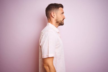 Zarif bir yaz tişörtü giyen yakışıklı bir adam pembe izole edilmiş arka planda, yan tarafa bakıyor, rahat poz veriyor, kendine güvenen bir gülümsemeyle doğal bir yüz ifadesi sergiliyor..