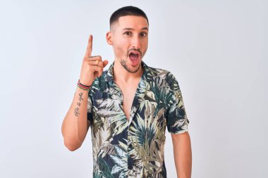 İzole edilmiş arka plan üzerinde Hawaii tişörtü giyen yakışıklı genç adam başarılı bir fikir işaret ediyor. Heyecanlı ve mutlu. Bir numara..