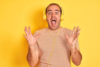 Müzik dinleyen genç bir adam, sarı arka plan üzerinde duran kulaklıkla çılgın ve başarıyı kollarını kaldırarak ve heyecanla haykırarak kutluyor. Kazanan konsept