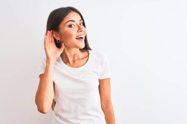 İzole edilmiş beyaz arka planda dikilen, rahat bir tişört giyen genç, güzel bir kadın. Kulağı kulağında, dedikoduları ve dedikoduları dinliyor. Sağırlık kavramı.
