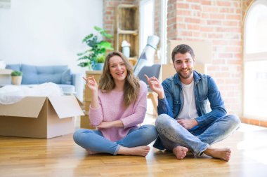 Genç ve güzel bir çift yeni bir eve taşınıyor. Yüzlerinde kocaman bir gülümsemeyle yerde oturuyor. Elleri ve parmaklarıyla kameraya bakıyor..